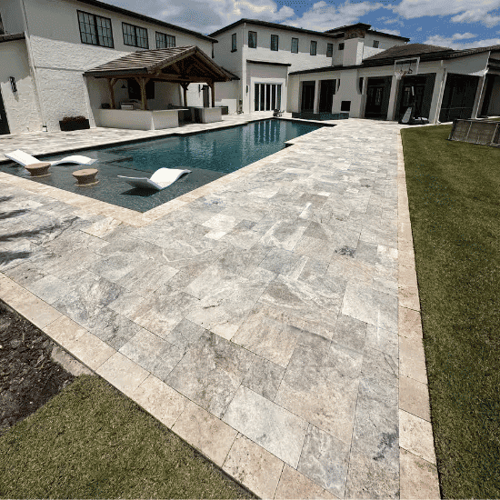 Luxury poolside view with stone patio and modern home exterior on a sunny day.