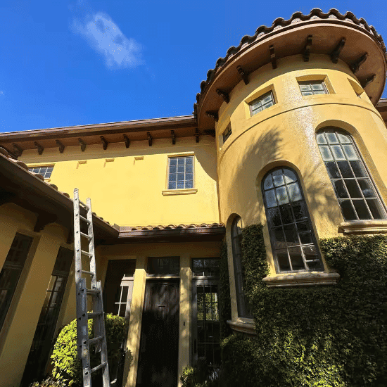Sunny view of a yellow house with a round tower and ladder for painting.